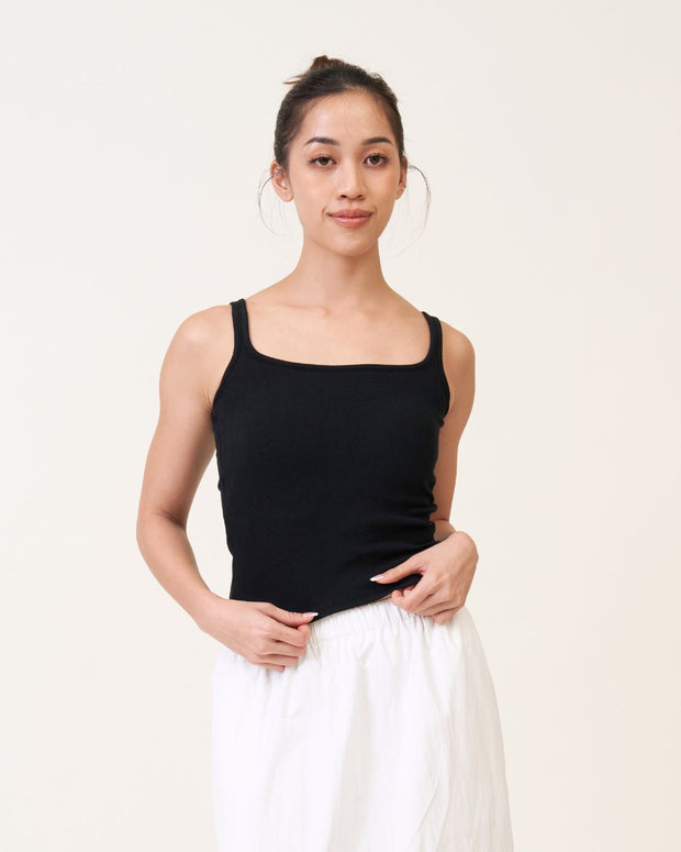 Woman wearing a black tank top and white pants against a plain background